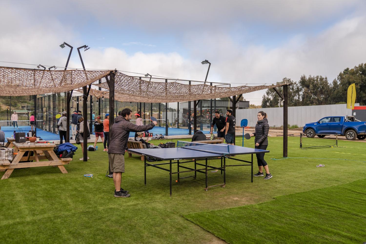 Terraza del club con mesa de ping pong, malla de sombra y gente mirando los partidos